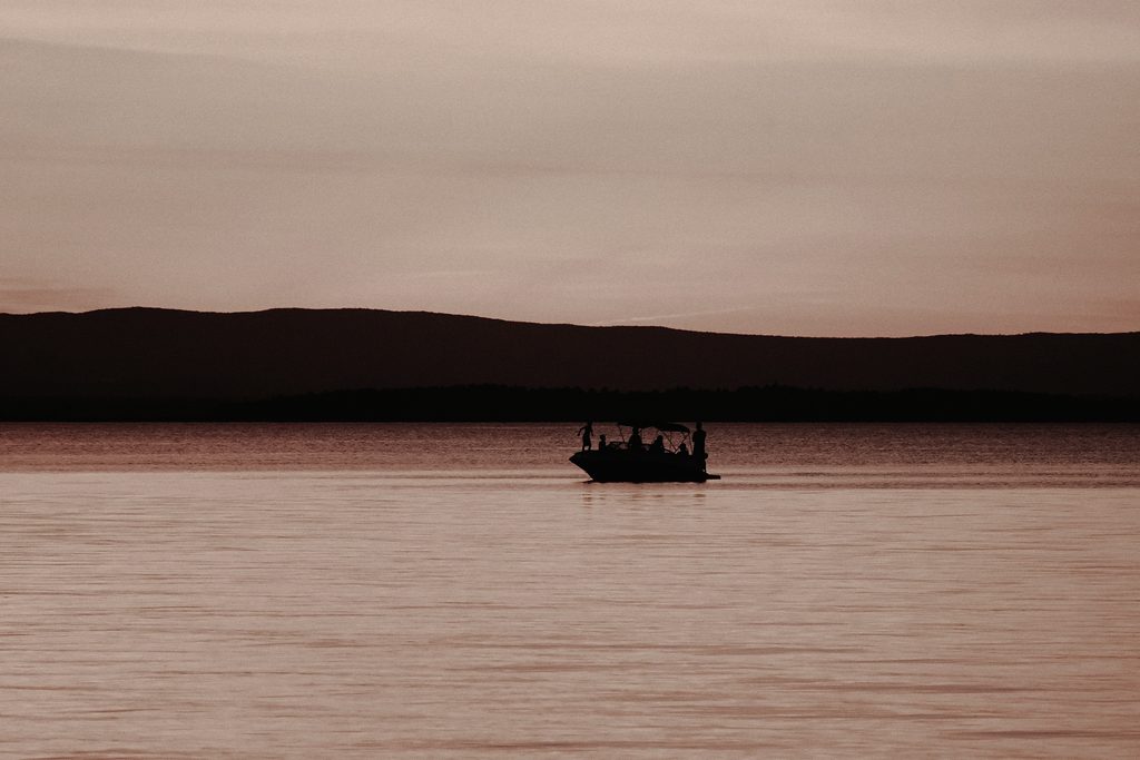 Anglers in a boat silhouetted on a wide prairie lake at last light